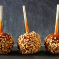 Three festive caramel apples with nuts against a dark slate background
